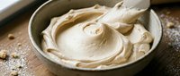 Creamy peanut butter swirl in ceramic bowl on rustic wooden surface, ready for cooking, baking, and food preparation projects.