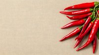 Fresh red hot chili peppers arranged in fan shape on beige linen textile background with copy space for text, food photography composition.