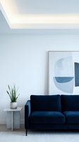 Modern living room interior with navy blue velvet sofa, potted plant on side table, and abstract artwork on white wall with contemporary ceiling lighting.
