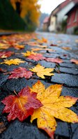 Wet maple leaves scattered on dark cobblestone street after rain, red and yellow autumn foliage against blurred background of residential houses on rainy fall day.