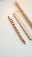 Rose gold ballpoint pen with cream leather case on white background, suitable for stationery, office supplies, and luxury product photography.