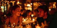 Young couple enjoying romantic candlelit dinner at restaurant, sharing intimate conversation with warm golden bokeh lights creating atmospheric ambiance.
