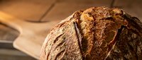 Freshly baked artisan sourdough bread loaf with crispy golden crust on wooden cutting board, rustic bakery style for culinary and food photography projects.