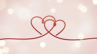 Two intertwined heart shapes formed by elegant red ribbon on soft pink bokeh background for romantic Valentine's Day wedding anniversary celebrations.