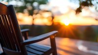 Wooden rocking chair silhouette on porch at sunset with golden sun rays peeking through, creating warm peaceful atmosphere for relaxation and mindfulness.