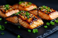 Grilled salmon fillets glazed with teriyaki sauce, garnished with sesame seeds and fresh chopped green onions on dark slate background for food photography and menus.