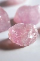 Raw rose quartz crystal on white background showcases natural pink hues and translucent mineral formation with rough edges and ethereal glow.