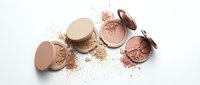 Broken makeup powder compacts with scattered cosmetic dust on white background for beauty and fashion design projects.