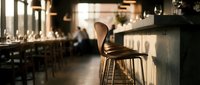 Wooden chair at bar counter in warm-lit restaurant or cafe interior with blurred background, suitable for hospitality, dining, and commercial design projects.