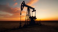 Oil pump jack silhouette against dramatic orange sunset sky in desert landscape, industrial crude oil extraction equipment at dusk creates striking contrast.