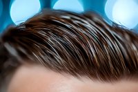 Close-up view of brown male hairstyle with styled waves against blurred blue bokeh background, showing modern trendy haircut details and texture.