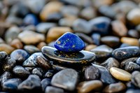 Vibrant blue lapis lazuli stone balanced on smooth river rocks creates zen harmony against natural pebble background, showcasing meditation and wellness concepts.