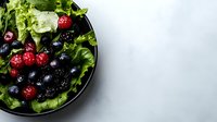 Fresh mixed berries with raspberries and blueberries served on green lettuce leaves in dark plate on light gray background, healthy eating concept.
