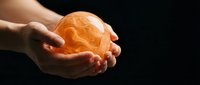 Two hands holding glowing orange sphere against dark background, symbolizing energy, innovation, and future technology for business and creative projects.