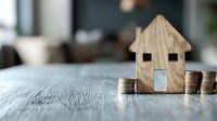 Wooden house model with coin stacks on table representing real estate investment, mortgage planning, property savings and home financing concepts.