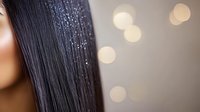 Straight dark hair with glitter sparkles on strands against blurred bokeh background, close up view of shiny healthy hairstyle with festive shimmer effect.
