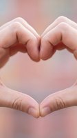 Hands forming a heart shape against a soft pink blurred background, symbolizing love, care, and compassion for Valentine's Day or health concepts.