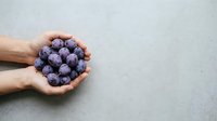 Fresh blueberries held in cupped hands against neutral background, suitable for food, nutrition, healthy eating, and organic produce marketing materials.