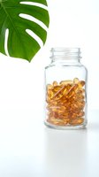 Glass jar filled with golden amber supplement capsules isolated on white background with fresh green monstera leaf, suitable for health, wellness, vitamin and nutritional product packaging and marketing.
