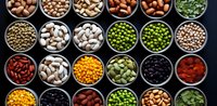 Variety of colorful legumes, pulses, nuts and seeds in metal bowls arranged in rows on dark background, top view composition for healthy eating and cooking.