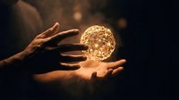 Hands holding glowing geometric sphere with warm light emanating from intricate wireframe structure against dark background creating magical atmosphere.
