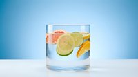Refreshing infused water with citrus slices and grapefruit in clear glass on white surface against blue background for healthy lifestyle concepts.