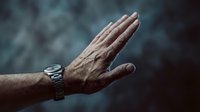 Mature man's hand with wristwatch raised in stop gesture against blurred background. Suitable for rejection, refusal, pause, and communication concepts.