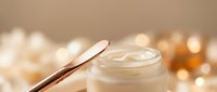 Luxury skincare cream jar with golden spatula on warm beige background with soft bokeh lights for premium beauty and cosmetic product advertising.