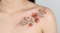 Delicate floral tattoo with orange blooms on woman's shoulder blade showcasing botanical art and feminine body modification in watercolor style.