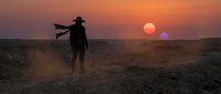 Silhouette of cowboy with flowing cape standing on desert landscape during dramatic sunset with orange sky for western themed projects.