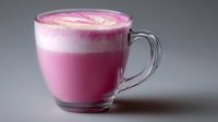 Pink beetroot latte with foam art in clear glass mug on gray background, trendy healthy drink featuring vibrant color and creamy texture.