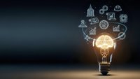 Glowing light bulb with business icons floating above representing innovation, creativity and entrepreneurial ideas for corporate strategy and growth.