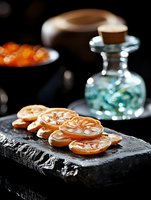Candied orange slices arranged on dark stone plate with decorative glass bottle, moody food photography with selective focus and natural lighting.