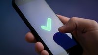 Close-up of hand holding smartphone displaying glowing green checkmark symbol on dark blue background, representing approval, confirmation, success, and digital validation for app design.