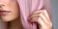 Young Asian woman with pastel pink hair touching her silky smooth strands against blurred background, showcasing modern hair coloring and styling trends.