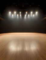 Empty stage with bright spotlight illumination and wooden floor in dark theater space, dramatic lighting creates atmospheric performance environment.