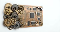 Circuit board with vintage brass and metal gears spilling out, representing fusion of old mechanical engineering with modern digital technology on white background.