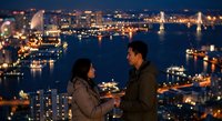 Romantic couple enjoying city skyline view at night with illuminated buildings and harbor lights creating perfect evening atmosphere for dating.