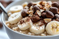 Creamy oatmeal bowl topped with fresh banana slices, chocolate shavings, nuts and seeds for healthy breakfast. Close up macro food photography.