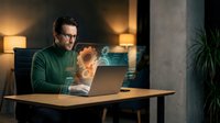 Professional Caucasian man in green sweater working on laptop at modern home office desk with warm ambient lighting and coffee steam rising from mug.