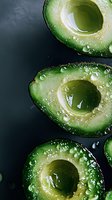Fresh cut avocado halves with water droplets on dark background, macro photography showing detailed texture and natural moisture of ripe fruit.