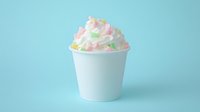 Colorful marshmallow pieces in white paper cup against pastel blue background. Minimalist food photography with soft candy dessert topping for creative design.
