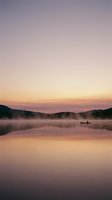 Solitary fisherman in small boat on misty lake at dawn, surrounded by forested hills under soft purple and golden sky, reflecting on calm water surface.
