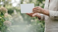 Mature man in light beige linen shirt holding blank white card outdoors with blurred green foliage background, suitable for business messaging and promotional campaigns.