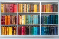 Colorful vintage books arranged by color spectrum on white bookshelf, creating rainbow pattern of leather-bound volumes for home library or bookstore display.