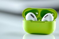 Bright lime green wireless earbuds charging case with white earphones on light background with soft shadow reflection, modern audio technology concept.