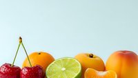 Fresh colorful fruits including cherries, orange, lime, tangerine and mango arranged on clean white background for healthy eating and nutrition concepts.