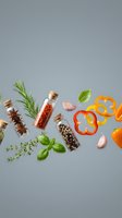 Spices in glass bottles with cork lids, fresh herbs, garlic, and colorful bell peppers arranged on a gray background for food design.