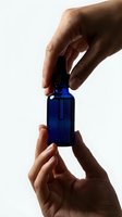 Hands holding a blue glass dropper bottle against white background, skincare serum or essential oil concept for beauty and wellness.