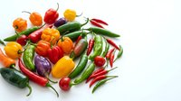 Assorted fresh chili peppers and bell peppers in red, orange, yellow, and green varieties arranged on white background for culinary and food styling projects.